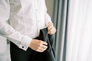 Damat otel odasında dikilirken elinde siyah bir ceket tutuyor. Kırpılmış. Yüzsüz. Yüksek kalite fotoğraf