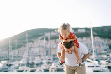 Omuzlarında gülümseyen küçük bir kız olan babam deniz kıyısında öne doğru eğiliyor. Yüksek kalite fotoğraf