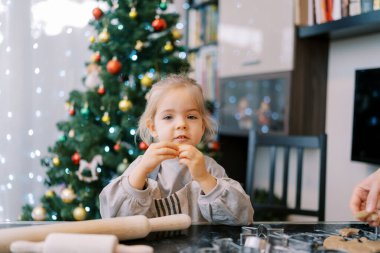Elinde kurabiyeyle küçük bir kız annesinin yanında oturmuş masada hamurunu yuvarlıyor. Yüksek kalite fotoğraf