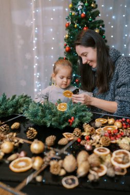 Küçük kız, annesine bir Noel çelengi için kuru portakala tutkal sürerken bakıyor. Yüksek kalite fotoğraf