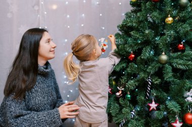 Annem, bir yılbaşı ağacına lama heykelciği asan küçük bir kıza bakıyor. Yüksek kalite fotoğraf