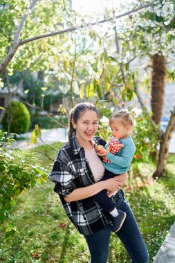 Kollarında küçük bir kızla gülümseyen anne bahçede bir yolda duruyor. Yüksek kalite fotoğraf
