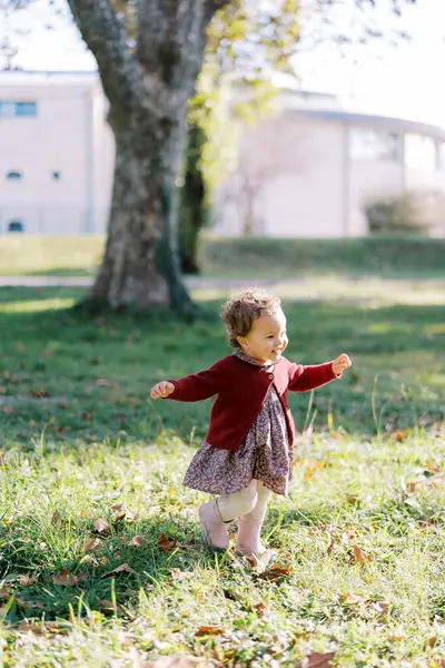 Küçük gülümseyen kız ellerini sallayarak yeşil çimlerde yürüyor. Yüksek kalite fotoğraf