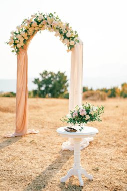 Bir buket çiçekli masa düğün kemerinin yanındaki açıklıkta duruyor. Yüksek kalite fotoğraf