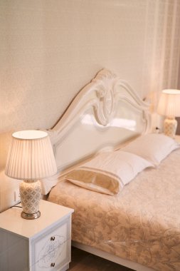 Otel odasındaki yatağın yanındaki komodinlerin üzerinde parlayan lambalar duruyor. Yüksek kalite fotoğraf