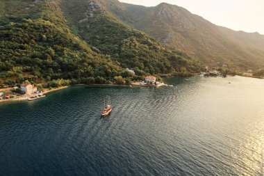 Yelkenli, körfez boyunca yeşil, ağaçlık bir dağ kıyısının arka planına doğru yelken açar. Drone. Yüksek kalite fotoğraf