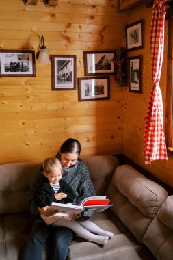 Annem, küçük bir kıza, tahta bir evin köşesindeki koltukta oturan bir kitap okuyor. Yüksek kalite fotoğraf