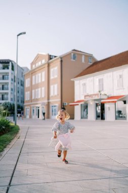 Pembe oyuncak tavşanlı küçük bir kız yolda ağzı açık koşuyor. Yüksek kalite fotoğraf