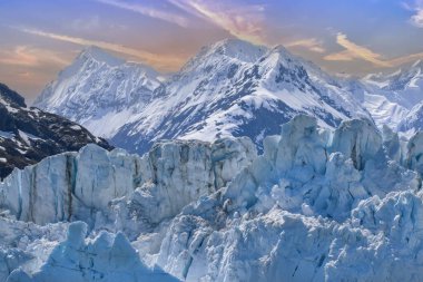 Alaska 'daki Buzul Koyu, mavi buzullar ve karla kaplı dağ zirvesi manzarası, görkemli gökyüzü.