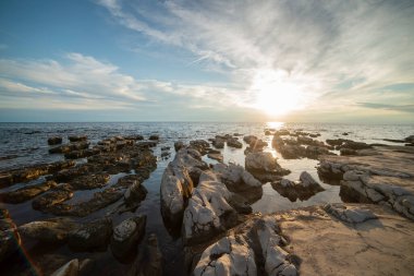 Umag şehrindeki Istrian yarımadasının kıyısında. Hırvatistan 'da deniz ve kayalar. Adriyatik Denizi kıyısında gün batımında. Kıyıdaki taşlar ve kayalar