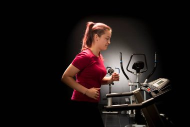 Young woman at the gym using walking treadmill on black background 