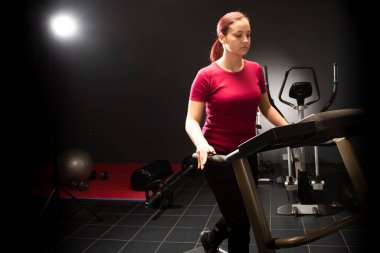 Young woman at the gym using walking treadmill on black background 