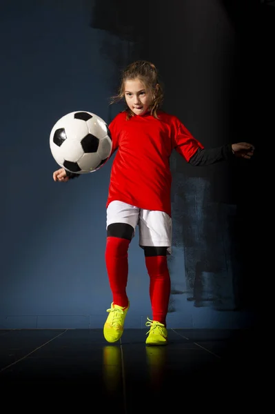 An elementary school girl is playing indoor soccer