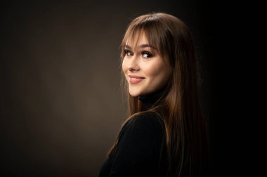 Young smiling girl looking at camera on isolated dark background. A beautiful female portrait.
