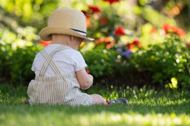 A boy with a hat on his head is sitting on the grass. A beautiful spring day.