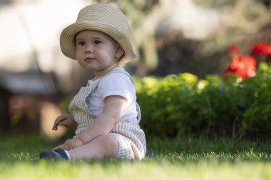 A boy with a hat on his head is sitting on the grass. A beautiful spring day.