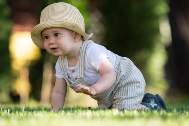A boy with a hat tries to crawl on the grass. A beautiful spring day.