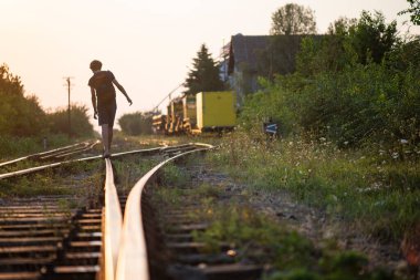 A boy with a backpack on his back walks on the tracks at dusk 