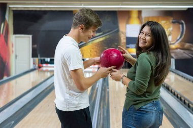 A guy and a beautiful and smiling girl bowling. They are having a good time.