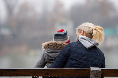 Soğuk bir sonbahar yağmurlu bir günde çocuklu bir anne bankta oturuyor.. 