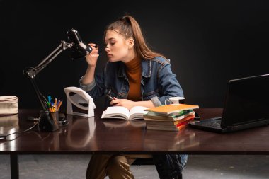 Masasında kitapları olan bir kız öğrenci. Kız masada oturuyor ve makyaj yapıyor. 