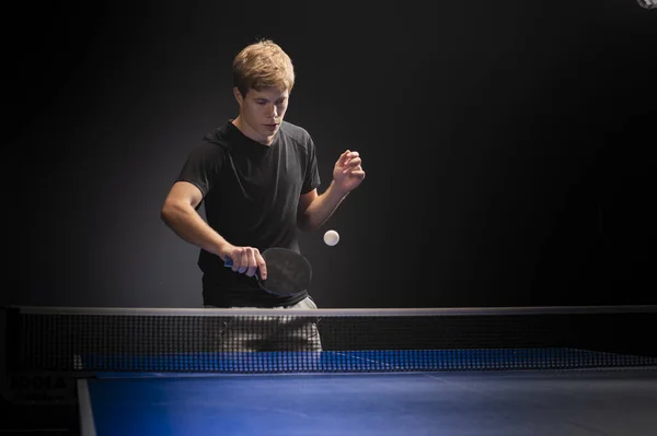 Portrait of young man playing tennis on black background