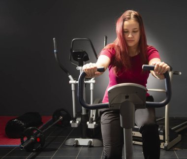 Girl doing cardio class at gym on exercise bike. Focus and weight loss motivation. Young woman training fitness workout on bicycle. 