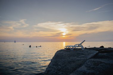 Hırvatistan 'da Adriyatik Denizi üzerinde gün batımları. Sahilde boş bir iskemle. Akdeniz ülkelerinin güzel dünyası Umag şehrindeki Istrian yarımadasının kıyısındaki Stone plajı..