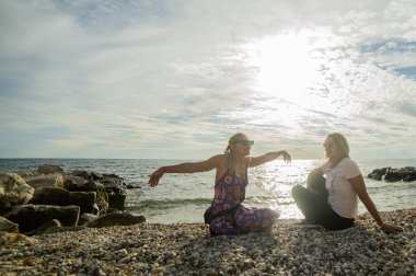 İki kadın çakıl taşı plajında oturur ve gün batımı gibi dinlenir. Ladin Gaj Plajı, Umag, Istrian Yarımadası, Hırvatistan