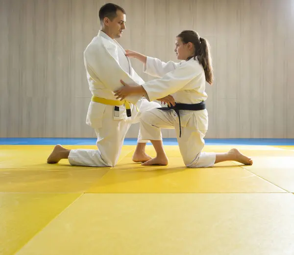 Yellow belt judo man in white judogi and young black belt judo girl in white judogi