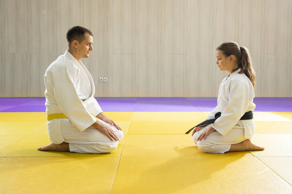 Желтый пояс дзюдо мужчина в белых дзюдоистах и молодая черная пояса девушка дзюдо в белых дзюдоистах на коленях 