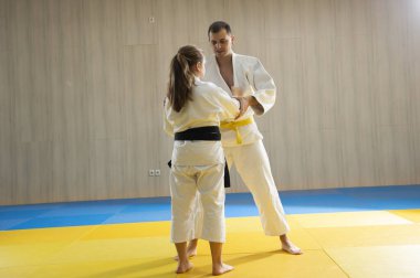 Beyaz judogi giyen genç sarı kuşak judo adamı ve beyaz judogi giyen genç siyah kuşak judo kızı.
