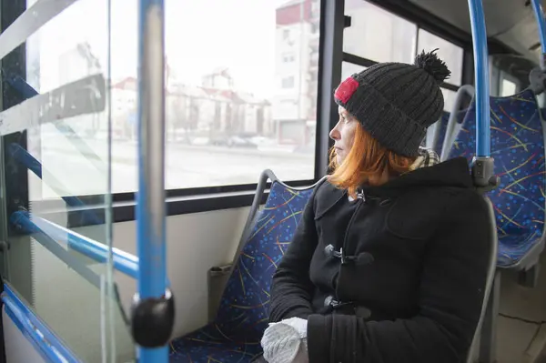 A middle-aged woman with red hair sits on a seat while riding a bus. A female passenger dreams on the bus.