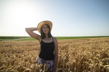 Sarı çayırlarda dikilen şapkalı mutlu kadın olgun altın buğdayla ellerini kaldırıyor. 