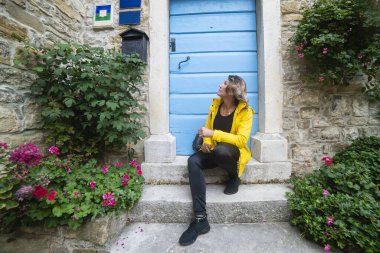 Kapının önündeki basamaklarda bir kadın oturuyor. Groznjan, sanatçılar şehri, Hırvatistan