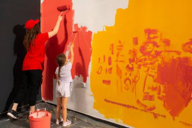 Anne ve kızı duvarı birlikte kırmızıya boyarlar. Ev yenilenmesi.