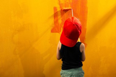 Sarı arka planda bir çocuk evin duvarında kırmızı bir silindir çiziyor.. 