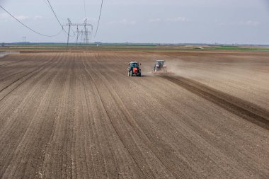İki traktör tarlada çalışıyor, toprağı ekime hazırlıyorlar, ekilebilir araziyi sürüyorlar.
