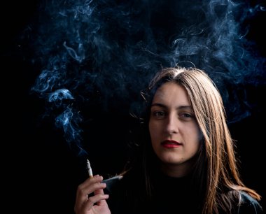 Siyah arka planda sigara içen genç bir kadın. Sigaraya odaklan. 