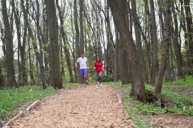 Genç bir kız ve oğlan baharda Beagle köpeğiyle ormanda koşuyorlar.