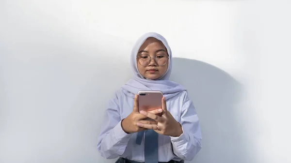 インドネシアの女子高生でグレーと白の制服を着て電話を真剣に見て保持します — ストック写真