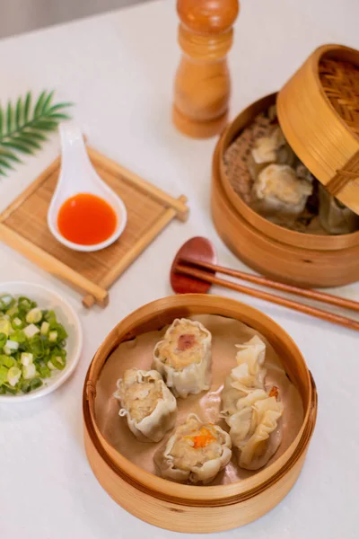 Steamed four flavor dumpling dimsum in traditional bamboo steamer with sauce and green leek. Close up food photography