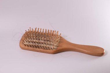 Beyaz bir bezin üzerindeki ahşap bir tarakta saç kaybı. Kırık saç, zarar görmüş saç telleri. Rambut rontok di sisir. Beyaz arkaplanda izole