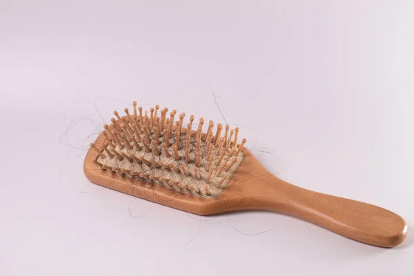 Beyaz bir bezin üzerindeki ahşap bir tarakta saç kaybı. Kırık saç, zarar görmüş saç telleri. Rambut rontok di sisir. Beyaz arkaplanda izole
