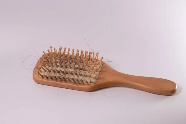 Beyaz bir bezin üzerindeki ahşap bir tarakta saç kaybı. Kırık saç, zarar görmüş saç telleri. Rambut rontok di sisir. Beyaz arkaplanda izole