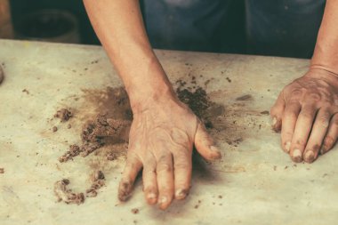 Çamur, su, bitki gibi gösterişli süsler yapmak ve her şeyi birbirine karıştırmak için elleriyle kil üzerinde çalışan bir zanaatkar..