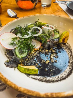 Kara karides akülü. Kabak, ızgara tortilla külleri, limon, soğan, turp ve yaban havucu. Kil kasede servis edilir..