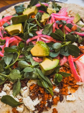 Su teresi, kırmızı soğan, cotija peyniri, fasulye ve avokado eşliğinde çekirge ve sucuklu Tlayuda..