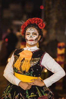 Ölü bayramı için giyinmiş ve bir katrina olarak nitelendirilen Meksikalı kadın, arkasında ölü bir adağı olan cempasuchil çiçekleri ve mumlarla.