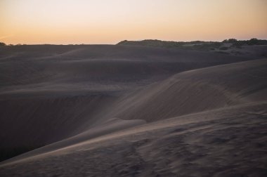 Kum tepelerinde gün batımı, güneşin son ışınlarından gelen pastel renklerle..